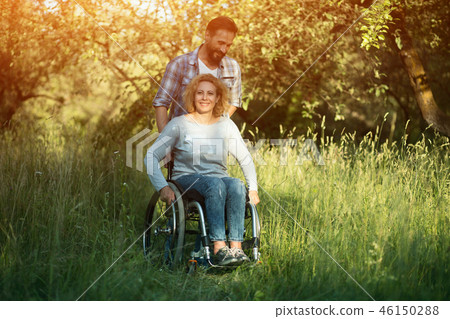 Smiling woman in wheelchair with husband in the park on sunny day 46150288