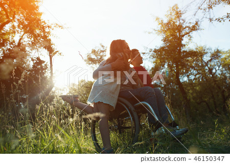 Woman in an armchair has fun with her husband and two children in park Woman in an armchair has fun with her husband and two children in park 46150347