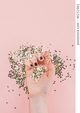 Woman hands covered golden stars confetti on pink Woman hands covered golden stars confetti on pink 46152901