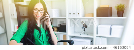 A young girl with glasses in the office speaks on the phone and holds a pencil in her hand. 46163094