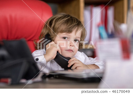 Little boy sits in the office in the chair and talking on the phone. Little boss. Little boy sits in the office in the chair and talking on the phone. Little boss. 46170049
