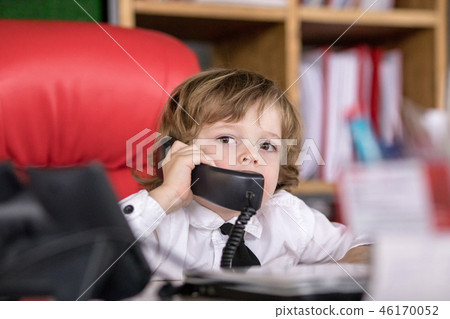 Little boy sits in the office in the chair and talking on the phone. Little boss. 46170052