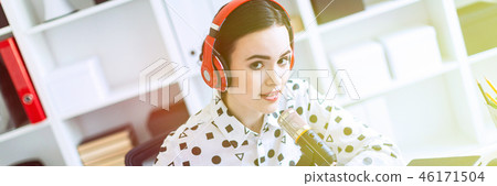 Beautiful young girl is sitting in headphones and with a microphone at the desk in the office. 46171504