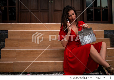 Fashionable girl in red drees holding leather snakeskin python bag, Elegant outfit. Model near the Fashionable girl in red drees holding leather snakeskin python bag, Elegant outfit. Model near the 46193201