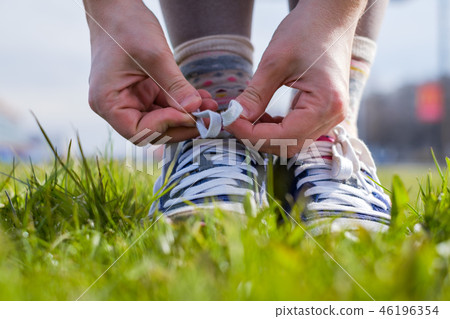 The girl ties up her shoelaces on sneakers. The girl ties up her shoelaces on sneakers. 46196354
