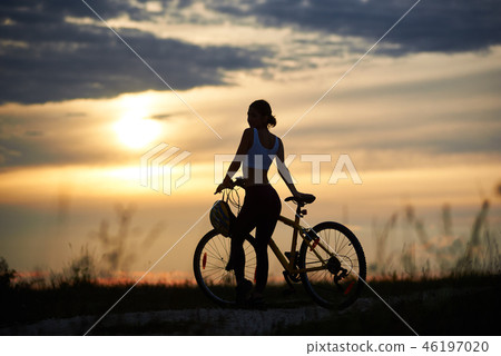 Slender, sporty woman standing near bike and posing. Slender, sporty woman standing near bike and posing. 46197020