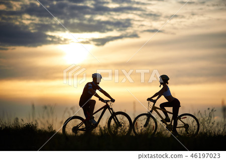 Two cyclists posing with bikes against amazing sky background. Two cyclists posing with bikes against amazing sky background. 46197023