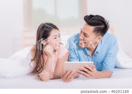 Happy Asian couple watching tablet in bed room Happy Asian couple watching tablet in bed room 46201180