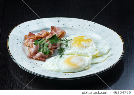Scrambled eggs and bacon in a white plate on a dark background close-up. Omelet Scrambled eggs and bacon in a white plate on a dark background close-up. Omelet 46204799