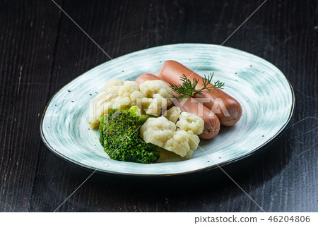 Broccoli, Cauliflower, sausage, in a white plate on a dark background. Breakfast, healthy food Broccoli, Cauliflower, sausage, in a white plate on a dark background. Breakfast, healthy food 46204806