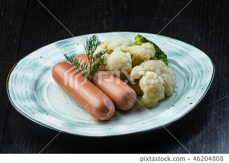 Broccoli, Cauliflower, sausage, in a white plate on a dark background. Breakfast, healthy food Broccoli, Cauliflower, sausage, in a white plate on a dark background. Breakfast, healthy food 46204808