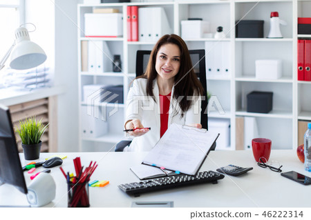 A young girl sitting in the office at a computer Desk and stretches forward a pen and a sheet. 46222314