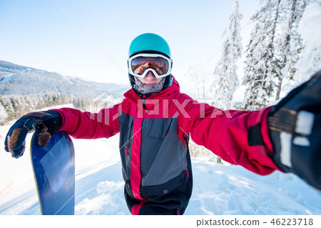 Shot of a man snowboarder taking a selfie, wearing helmet, skiing mask and colorful winter snowboard 46223718