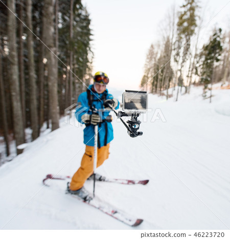 Skier man taking selfie with stick over forest on the winter resort. Focus on his camera 46223720