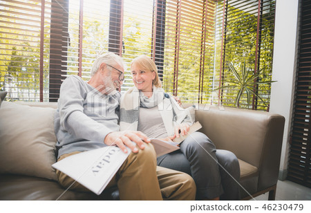 Senior couple sitting at sofa reading a book. 46230479