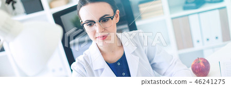 A beautiful young girl in a white robe is sitting at the table and typing on the keyboard. 46241275