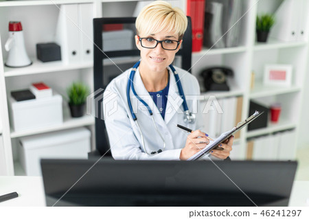 A young girl in a white robe sitting at the table and fills out a document 46241297