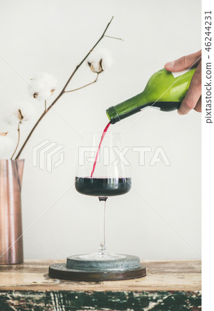 Red wine pouring from bottle in man's hand into wineglass Red wine pouring from bottle in man's hand into wineglass 46244231