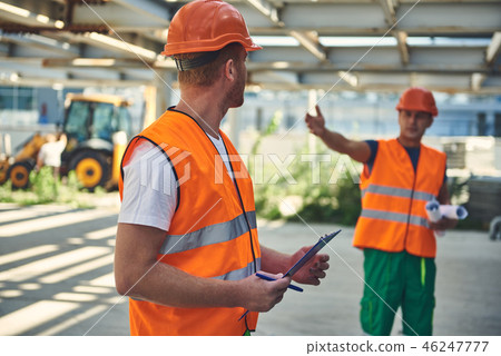 Workers in orange form are communicating at the construction site 46247777