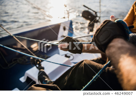Close-up of male hands in gloves pulling rope of sailboat while mooring yacht and sitting with Close-up of male hands in gloves pulling rope of sailboat while mooring yacht and sitting with 46249007