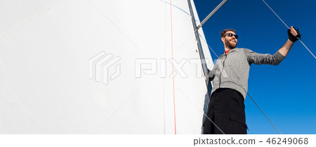 Yacht captain with a beard stands on sail boom on a sailing yacht, holding the rope in his hand and 46249068