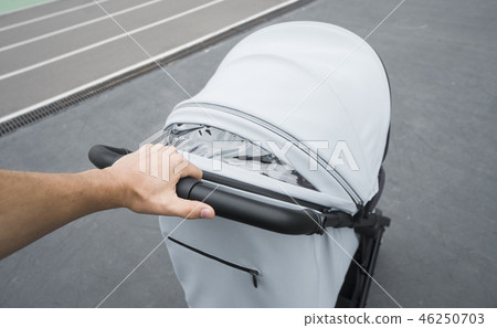 Young woman strolling a carriage outdoor. Closeup shot of male hands with grey stroller handle 46250703