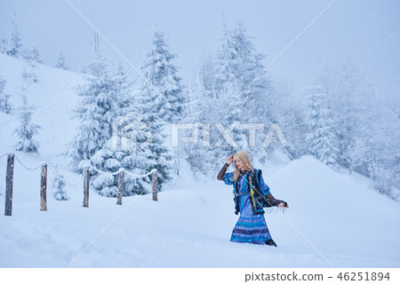 Attractive blond girl in long blue dress, embroidered warm sleeveless fur coat outdoor in deep snow. 46251894