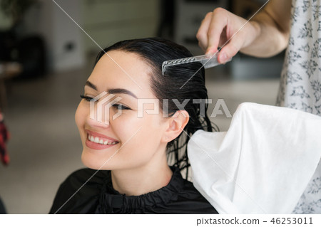Close up of a young happy beautiful woman smiling to the camera while professional hairdresser 46253011