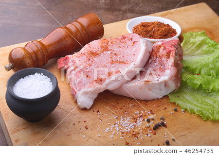 Raw chop on a rustic cutting board with salt, pepper and grinder for spices . for copy space. Top 46254735