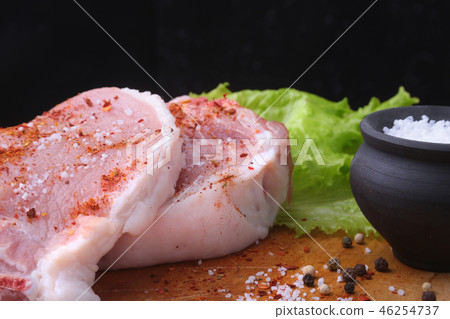 Raw steak on rustic cutting board with salt, pepper and grinder for spices. Black Background for Raw steak on rustic cutting board with salt, pepper and grinder for spices. Black Background for 46254737