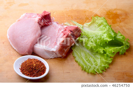 Raw chop on a rustic cutting board with salt, pepper and grinder for spices . for copy space. Top 46254750