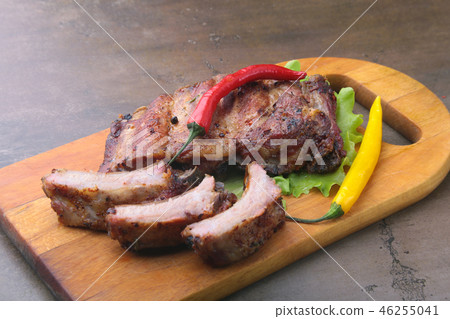 grilled barbecued ribs with lettuce leaves, hot chili pepper and sauce on wooden cutting board. 46255041
