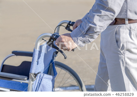 Men's hand pressing a wheelchair up. Care, assistance, welfare, old age, disability image Men's hand pressing a wheelchair up. Care, assistance, welfare, old age, disability image 46258829
