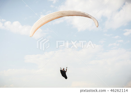 Professional paraglider in a cocoon suit flies high above the ground against the sky Professional paraglider in a cocoon suit flies high above the ground against the sky 46262114
