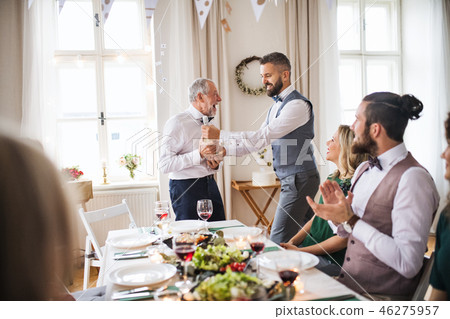 A man giving a bottle of wine to his father on indoor birthday party, a celebration concept. A man giving a bottle of wine to his father on indoor birthday party, a celebration concept. 46275957