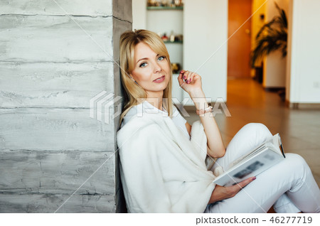 Young woman reading book on floor near light wall Young woman reading book on floor near light wall 46277719