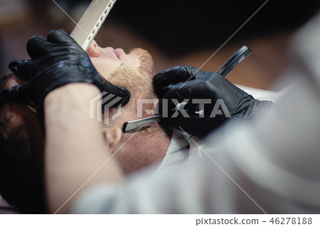 Hairdresser in black gloves shaves with a straight razor beard 46278188