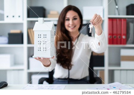 A young girl sitting at a table and holding a house and keys. 46279584