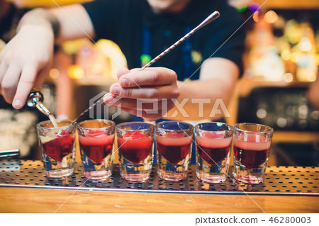 Bartender is pouring tequila into glass against the background of the bar. 46280003