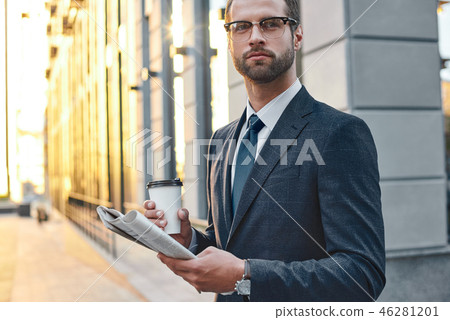 Surprised businessman in suit and glasses holding a paper cup and reading business newspaper in his 46281201