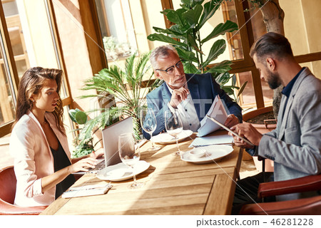 Business lunch. Three people in the restaurant sitting at table brainstorming on project using 46281228