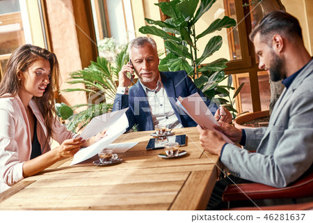 Business lunch. Three people in the restaurant sitting at table working on marketing strategy while Business lunch. Three people in the restaurant sitting at table working on marketing strategy while 46281637