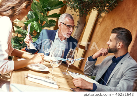 Business lunch. Three people in the restaurant sitting at table negotiating about contract. Team Business lunch. Three people in the restaurant sitting at table negotiating about contract. Team 46281648