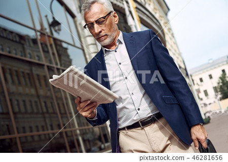 Reading the latest news. Confident senior man in casual suit reading newspaper while standing Reading the latest news. Confident senior man in casual suit reading newspaper while standing 46281656