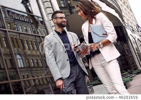 Using gadget. Two young business people standing outside on the city street using digital tablet Using gadget. Two young business people standing outside on the city street using digital tablet 46281659