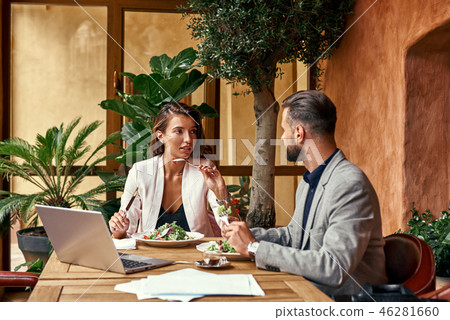 Business lunch. Man and woman sitting at table at restaurant eating healthy fresh salad discussing Business lunch. Man and woman sitting at table at restaurant eating healthy fresh salad discussing 46281660