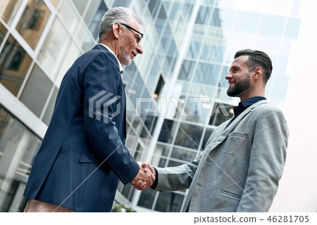 Meeting is started. Young and senior smiling businessmen shaking hands together while standing 46281705