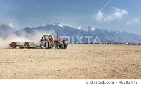 Tractor pulling heavy metal roller over dry field 46282472