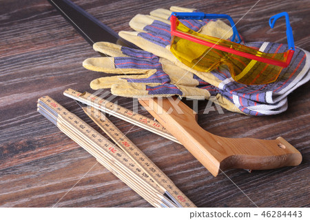 Orange hard hat, safety glasses, gloves, saw and measuring tape on wooden background. you can place Orange hard hat, safety glasses, gloves, saw and measuring tape on wooden background. you can place 46284443