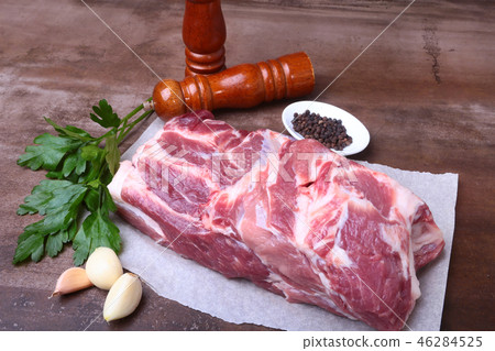 Raw pork neck chop meat with parsley herb leaves, grinder for spices and garlic on a stone Raw pork neck chop meat with parsley herb leaves, grinder for spices and garlic on a stone 46284525